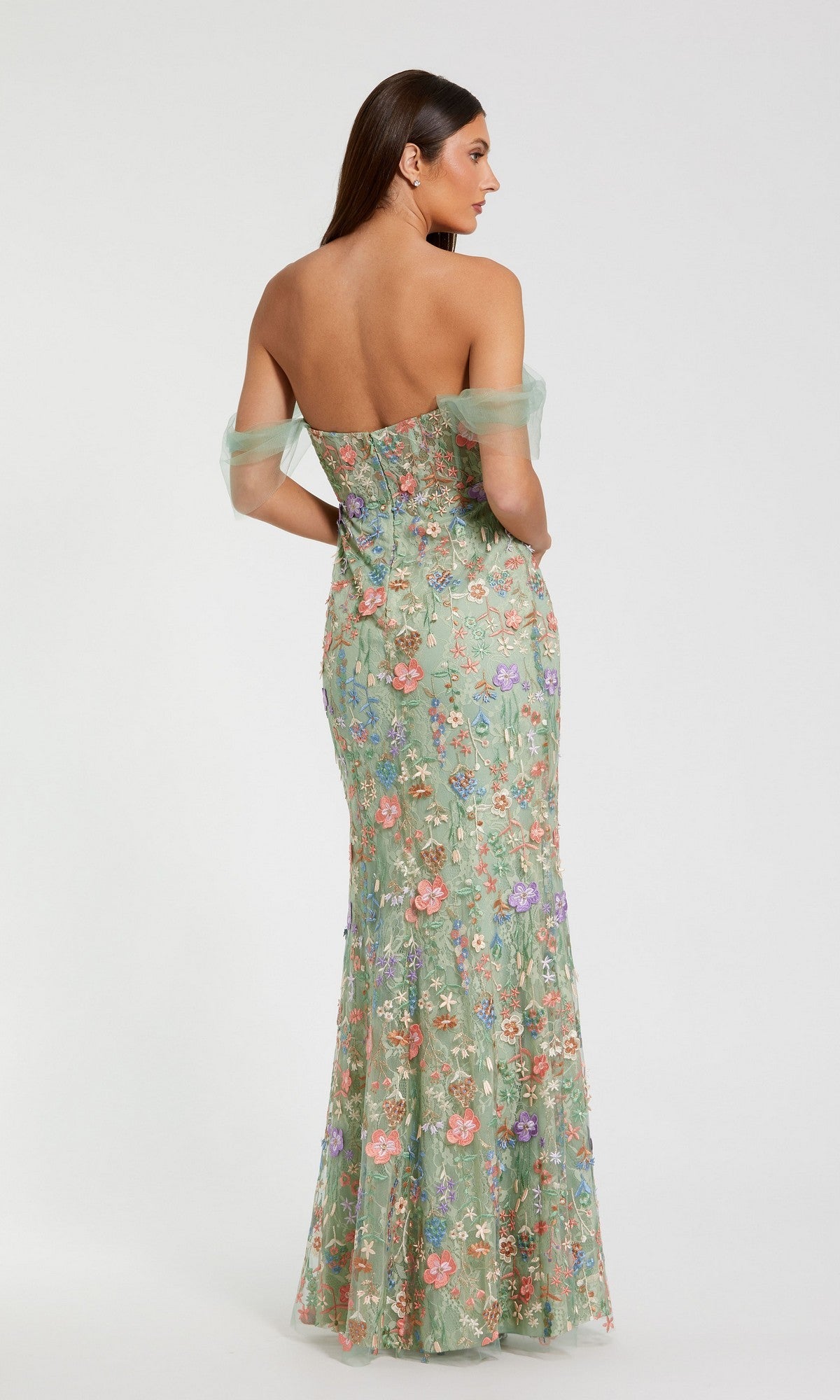A woman stands with her back to the camera, wearing the Mac Duggal 68809 long formal dress in light green. The gown features off-the-shoulder sleeves, floral embroidery, and a fitted corset bodice.